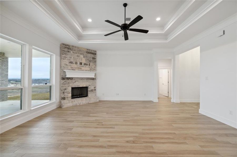 Unfurnished living room with ceiling fan, crown molding, a raised ceiling, light hardwood / wood-style floors, and a brick fireplace