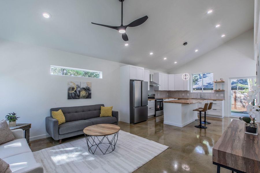 Living room with recessed lighting, high vaulted ceiling, concrete flooring, and ceiling fan