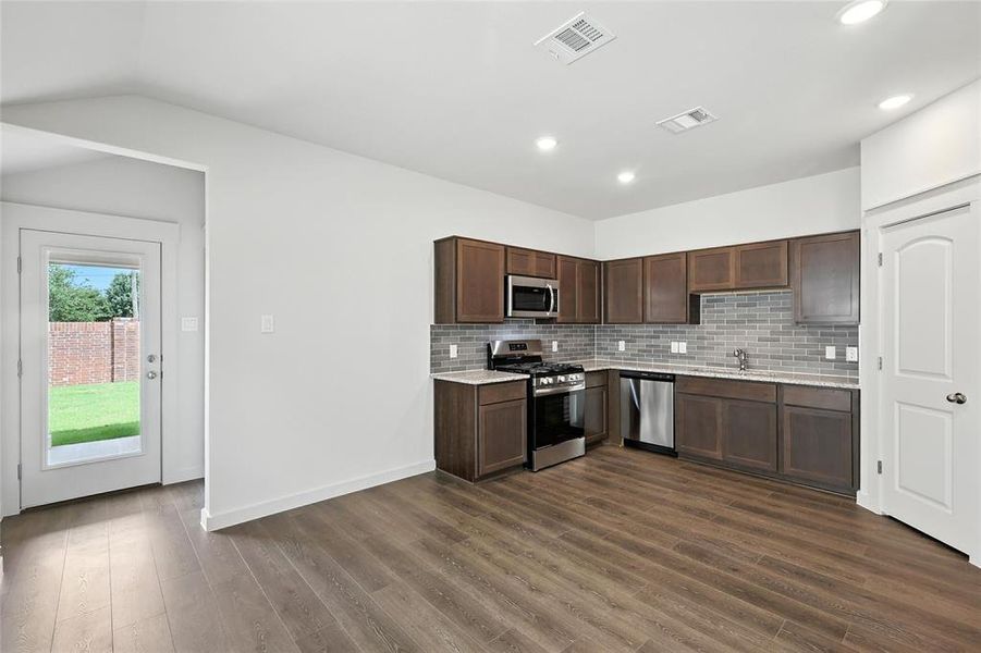 Kitchen with stainless steel appliances, dark wood-style floors, tasteful backsplash, dark brown cabinetry, and vaulted ceiling Kitchen with stainless steel appliances, dark wood-style floors, tasteful backsplash, dark brown cabinetry, and vaulted ceiling
