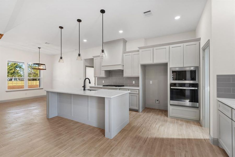 Kitchen with stainless steel appliances, decorative light fixtures, decorative backsplash, light wood-style flooring, and recessed lighting