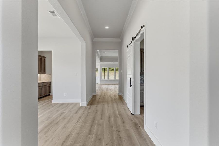 Hallway with a barn door, light wood-type flooring, ornamental molding, and recessed lighting