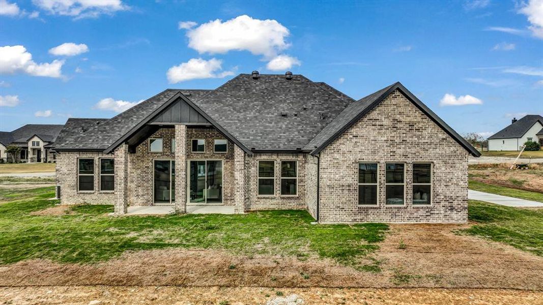 Back of house with brick siding, a yard, roof with shingles, and board and batten siding