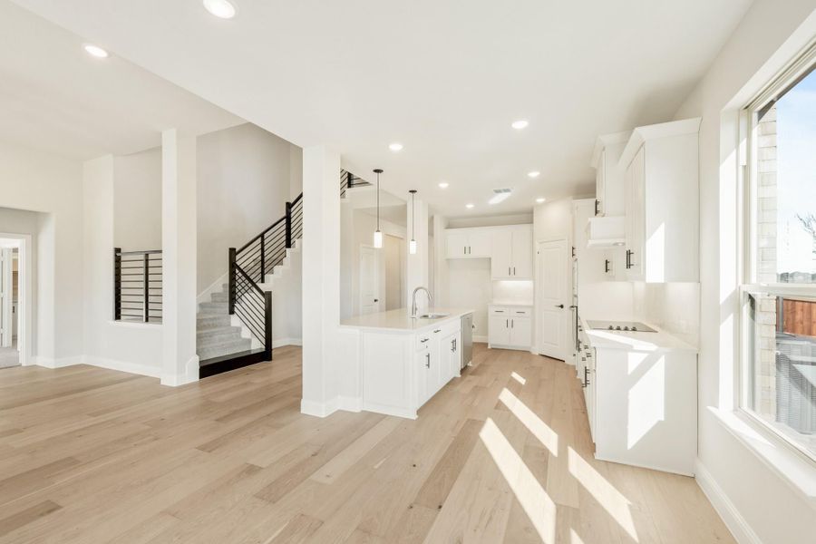 Open-concept kitchen with white cabinets, center island, and light hardwood floors, with staircase visible in background.