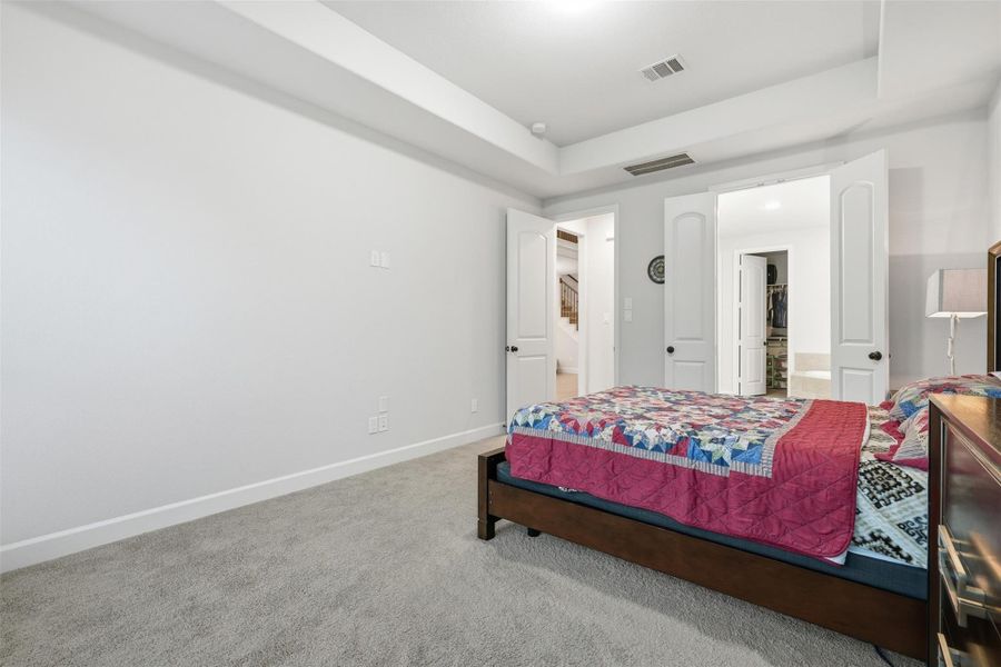 This photo showcases a bright, spacious bedroom with neutral walls and carpet. It features a large bed with a colorful quilt, a ceiling light, and double doors leading to a walk-in closet, adding functionality and comfort. This photo showcases a bright, spacious bedroom with neutral walls and carpet. It features a large bed with a colorful quilt, a ceiling light, and double doors leading to a walk-in closet, adding functionality and comfort.