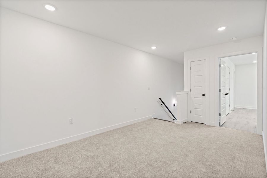 Recessed lighting throughout, plush carpeting, white interior doors with black hardware, and a staircase with a black handrail