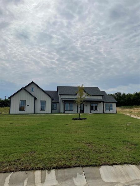 Modern farmhouse style home with a front lawn, board and batten siding, and roof with shingles