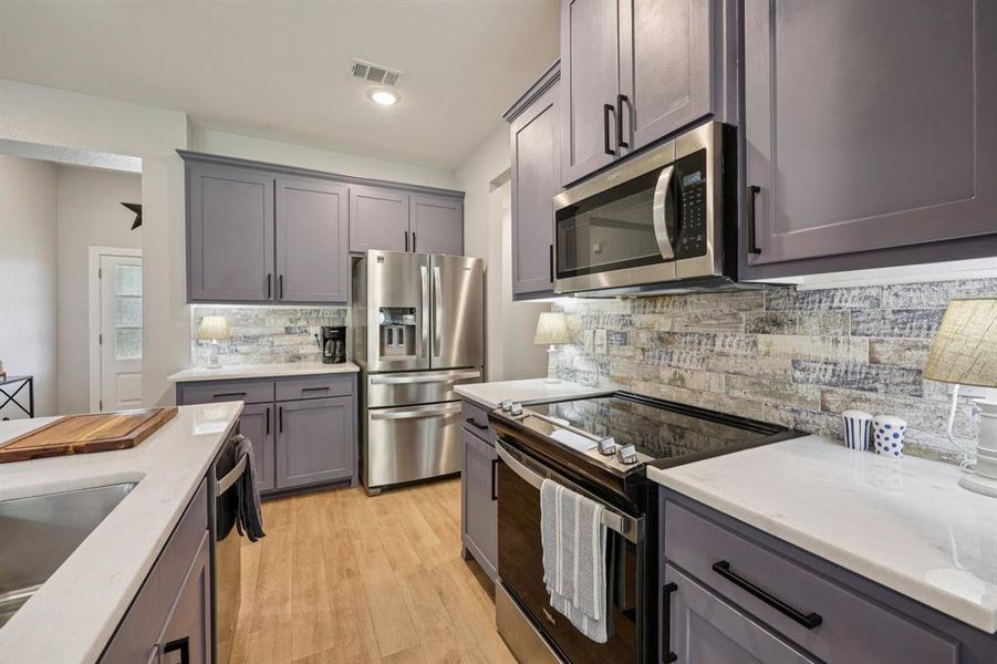 Kitchen with stainless steel appliances, tasteful backsplash, light wood finished floors, light stone counters, and gray cabinetry Kitchen with stainless steel appliances, tasteful backsplash, light wood finished floors, light stone counters, and gray cabinetry