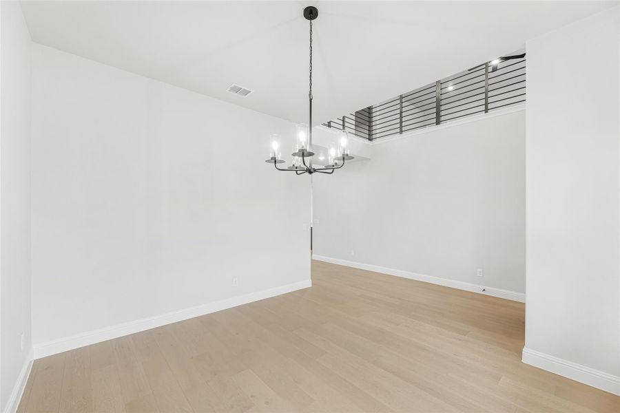 Empty dining room with light wood floors, black chandelier, and second-floor railing overlook above