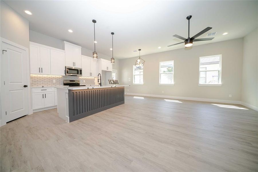 Kitchen with an island with sink, open floor plan, white cabinets, hanging light fixtures, and light wood-type flooring Kitchen with an island with sink, open floor plan, white cabinets, hanging light fixtures, and light wood-type flooring