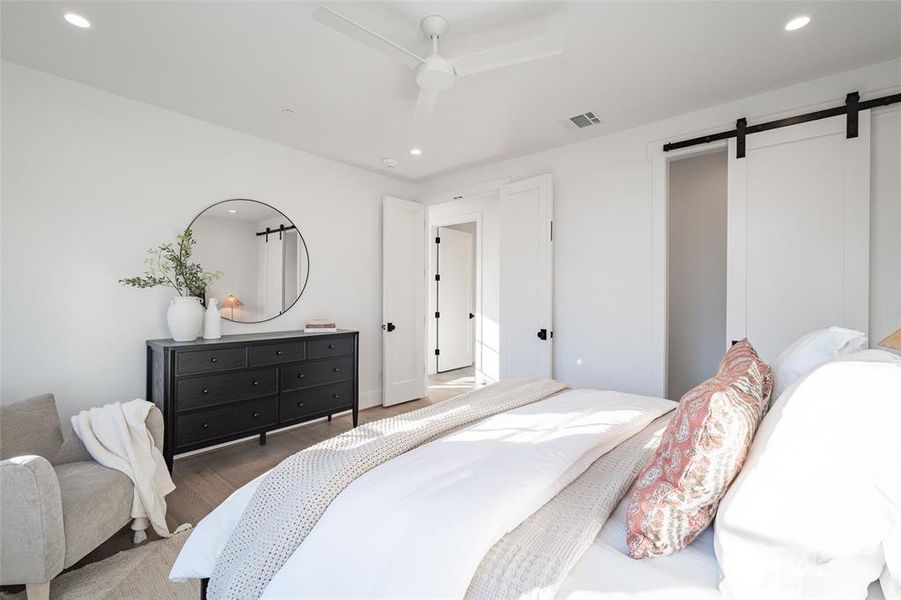 Bedroom featuring a barn door, ceiling fan, and dark wood-type flooring