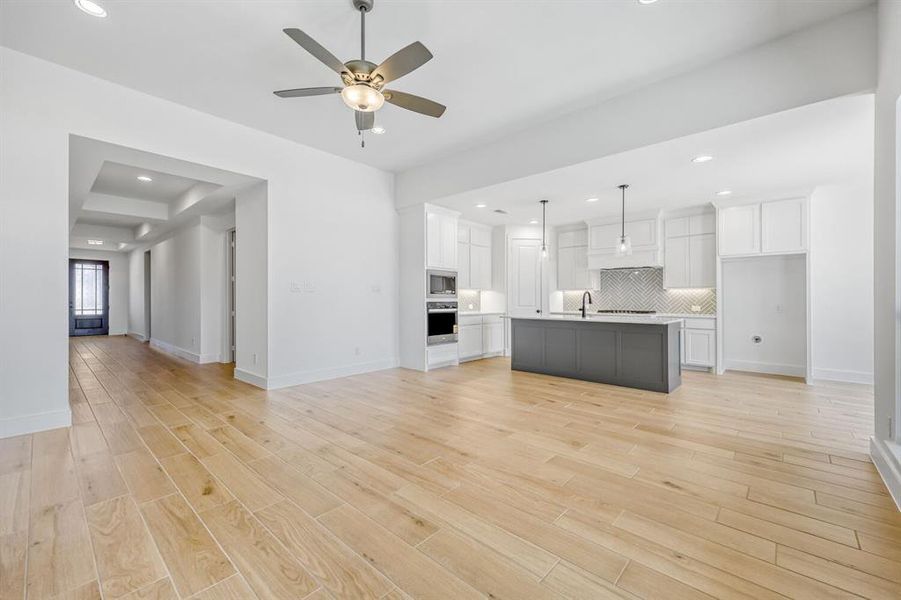 Two tone kitchen featuring open floor plan, a center island with sink, a ceiling fan, light countertops, and light wood-type flooring