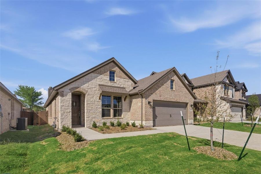 French country style house with concrete driveway, stone siding, a front yard, brick siding, and a garage