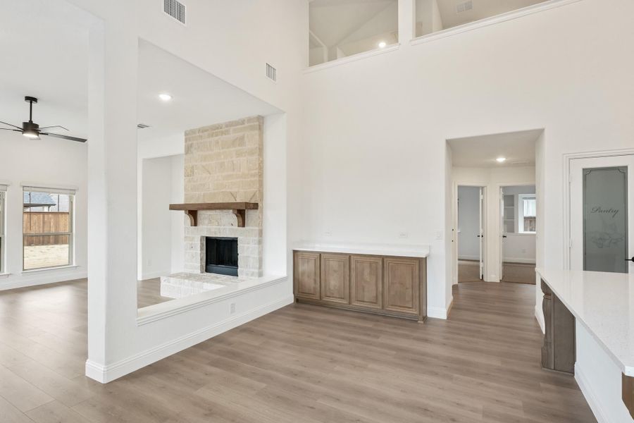 Open living area with two-story ceilings, stone fireplace, wood mantel, and hardwood floors Open living area with two-story ceilings, stone fireplace, wood mantel, and hardwood floors