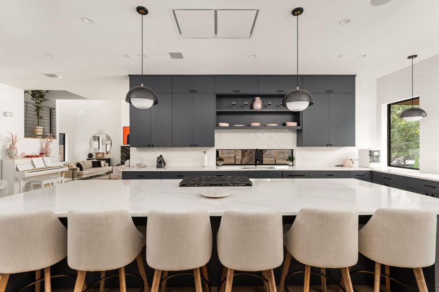 An open-concept kitchen boasts a large island with seating, dark cabinetry, and integrated cooktop, complemented by sleek pendant lighting. An open-concept kitchen boasts a large island with seating, dark cabinetry, and integrated cooktop, complemented by sleek pendant lighting.
