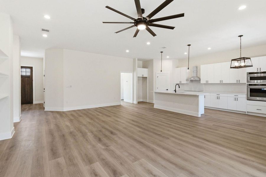An open concept living area transitions smoothly into a modern kitchen, boasting recessed and pendant lighting, and light wood-look flooring. An open concept living area transitions smoothly into a modern kitchen, boasting recessed and pendant lighting, and light wood-look flooring.
