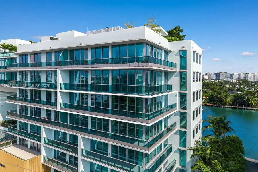 Modern multi-story building featuring white stucco facade, expansive floor-to-ceiling windows, wrap-around glass-railed balconies, and a rooftop terrace Modern multi-story building featuring white stucco facade, expansive floor-to-ceiling windows, wrap-around glass-railed balconies, and a rooftop terrace