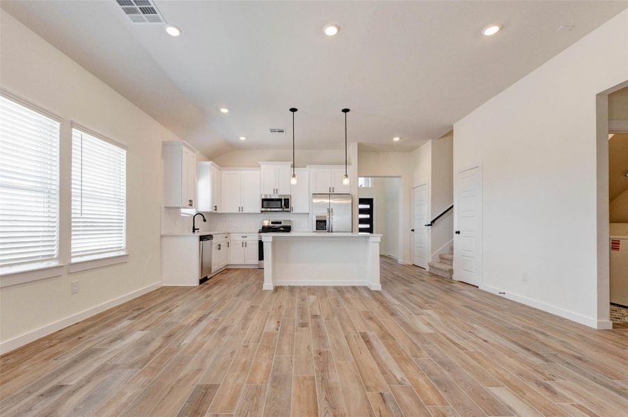 This expansive kitchen and dining space offers a bright, open layout perfect for gatherings. Featuring white cabinetry, sleek hardware, and stainless steel appliances, the kitchen exudes contemporary elegance. Large windows invite natural light, while the open floor plan allows for effortless interaction between cooking, dining, and relaxing areas.