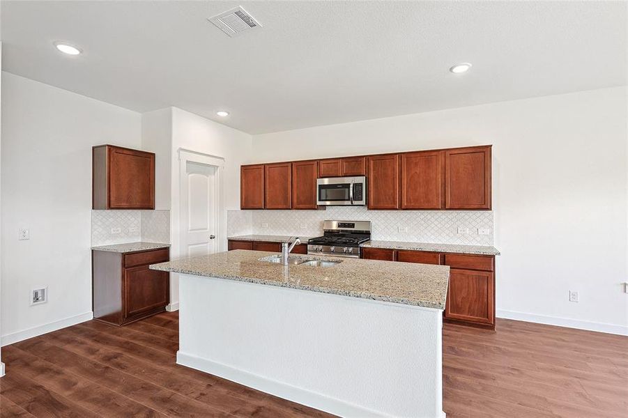 Kitchen with a center island with sink, appliances with stainless steel finishes, dark hardwood / wood-style flooring, and sink