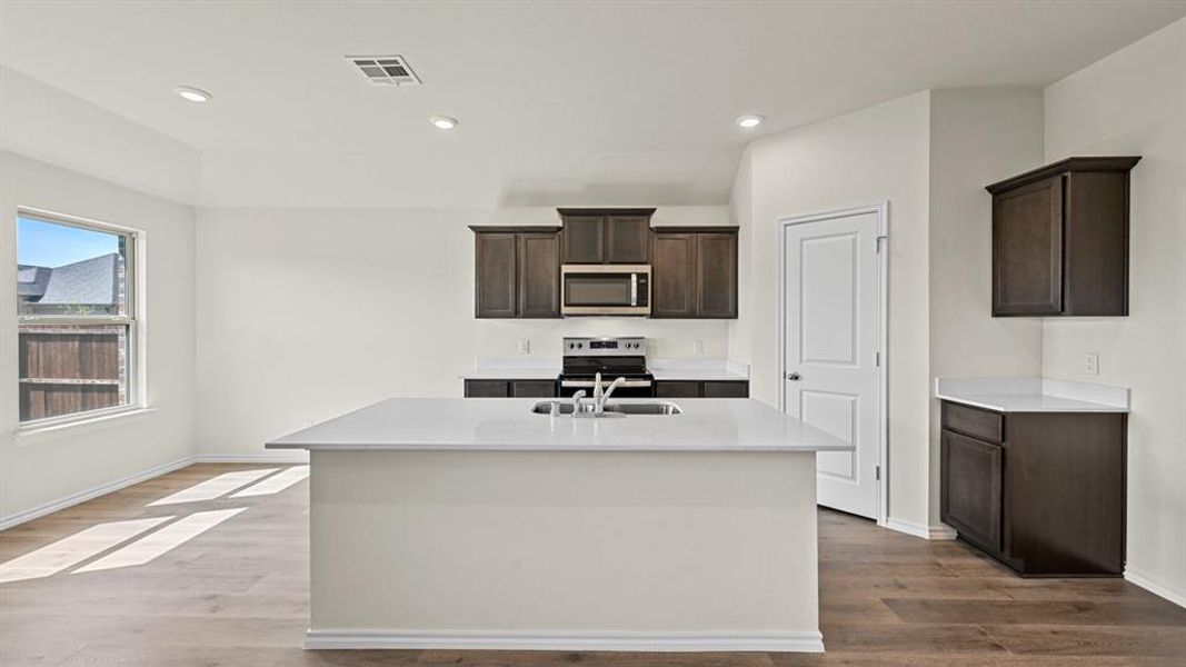 Kitchen featuring dark wood finish cabinets, stainless steel appliances, an island with sink, dark wood-type flooring, and recessed lighting