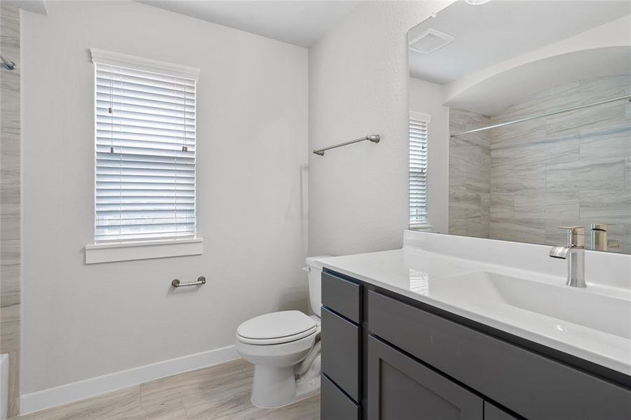 Secondary bathroom features light countertops and grey cabinets, neutral paint, shower/tub combo with tile surround, large mirror, tile floors, sleek fixtures and modern finishes, plenty of space to accommodate any visiting family or guests.