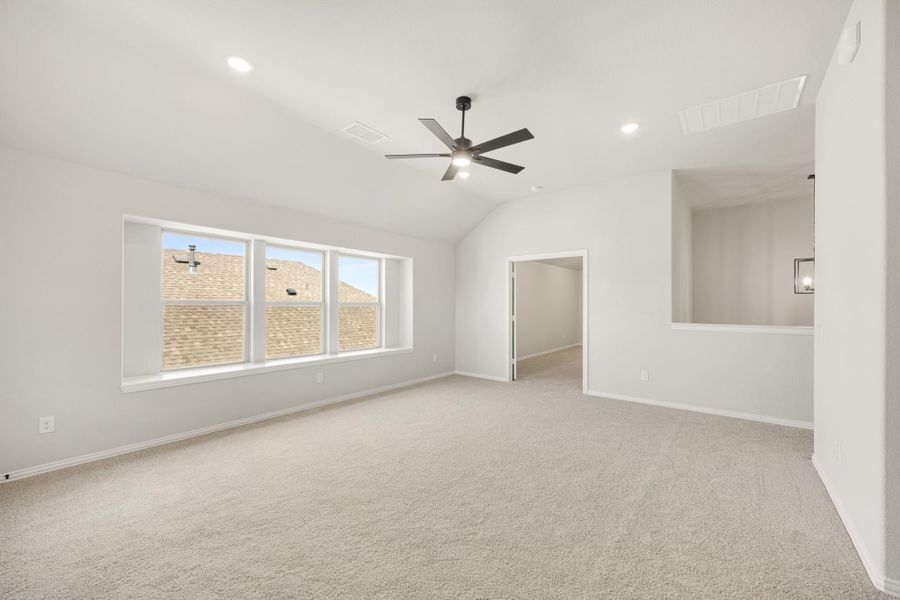Empty living room with vaulted ceiling, ceiling fan, carpet flooring, and large windows