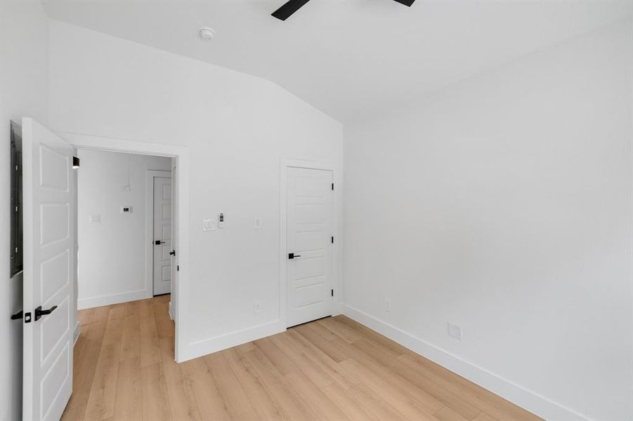 Empty room featuring vaulted ceiling, light wood finished floors, a ceiling fan, and a smoke detector