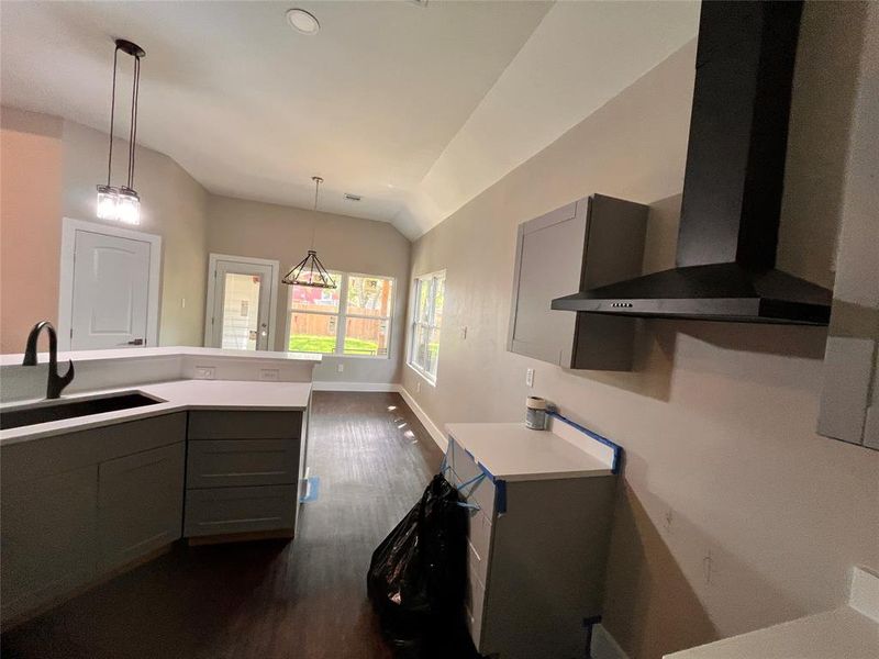 Kitchen featuring wall chimney exhaust hood, pendant lighting, sink, gray cabinets, and lofted ceiling