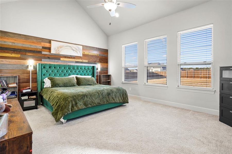 Bedroom with high vaulted ceiling, wood walls, light carpet, and a ceiling fan Bedroom with high vaulted ceiling, wood walls, light carpet, and a ceiling fan
