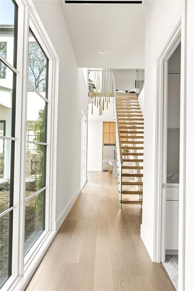 Hallway with light wood-finish flooring extending towards a floating staircase