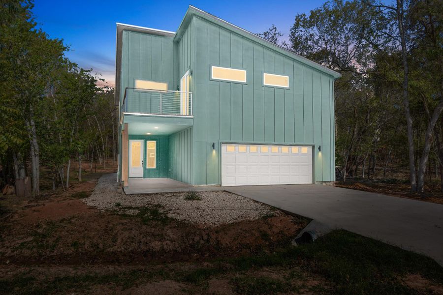 View of front of home featuring board and batten siding, a balcony, a garage, driveway, and a patio