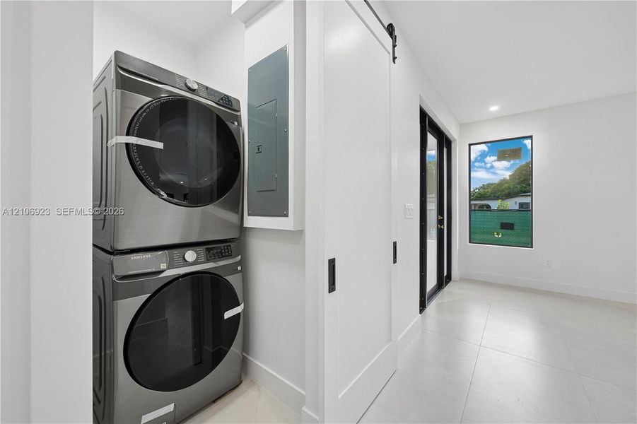 Laundry space featuring large-format tile flooring, a white sliding barn door with matte black hardware, and an exterior glass door with a black frame Laundry space featuring large-format tile flooring, a white sliding barn door with matte black hardware, and an exterior glass door with a black frame