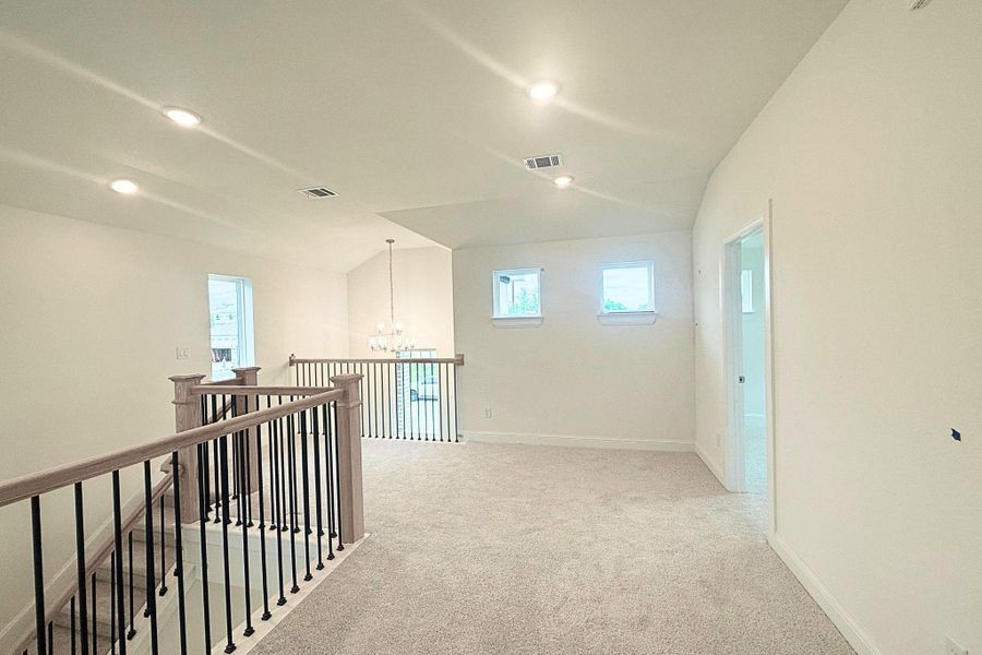 Spacious loft area featuring vaulted ceilings, recessed lighting, carpet flooring, and a decorative chandelier illuminating the railing below Spacious loft area featuring vaulted ceilings, recessed lighting, carpet flooring, and a decorative chandelier illuminating the railing below