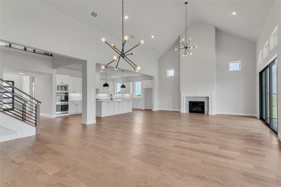 Unfurnished living room with a notable chandelier, sink, light hardwood / wood-style floors, and high vaulted ceiling