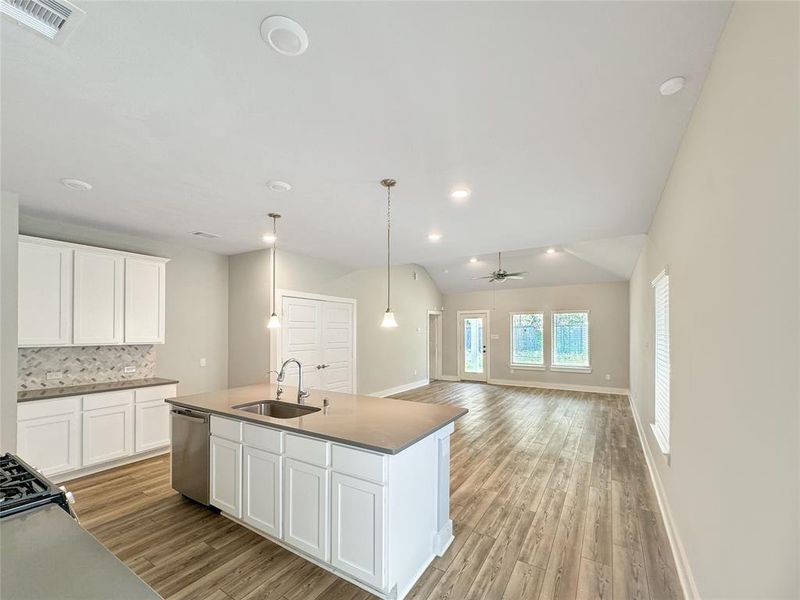 A modern kitchen with white cabinets, stainless steel appliances, and an island, opening into a spacious living area.