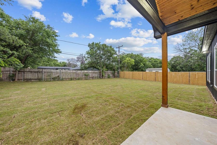 Expansive backyard featuring a manicured lawn, a solid wood fence, and a concrete patio Expansive backyard featuring a manicured lawn, a solid wood fence, and a concrete patio