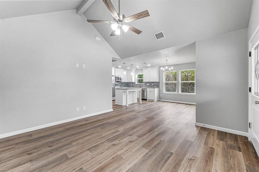 Unfurnished living room featuring a chandelier, ceiling fan, high vaulted ceiling, beam ceiling, and light wood-style flooring Unfurnished living room featuring a chandelier, ceiling fan, high vaulted ceiling, beam ceiling, and light wood-style flooring