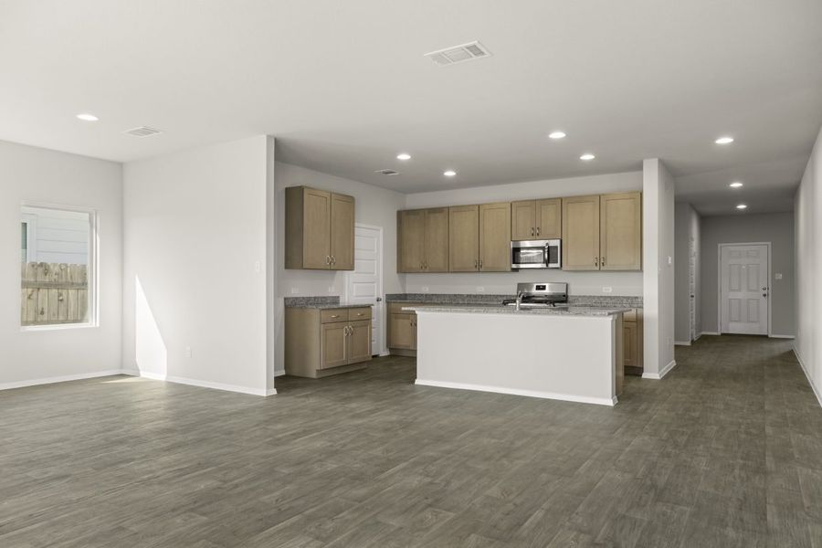 Image of home kitchen with light brown cabinets, center island, wood-look floors and white walls. Dining room on the left and entry way to front door on the right
