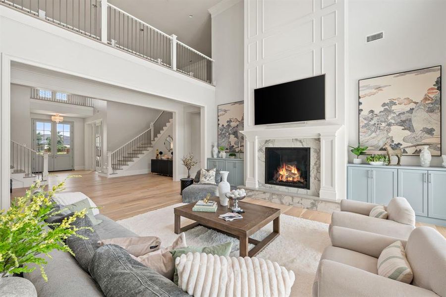 Living room featuring light wood-style flooring, stairway, a premium fireplace, and a towering ceiling Living room featuring light wood-style flooring, stairway, a premium fireplace, and a towering ceiling