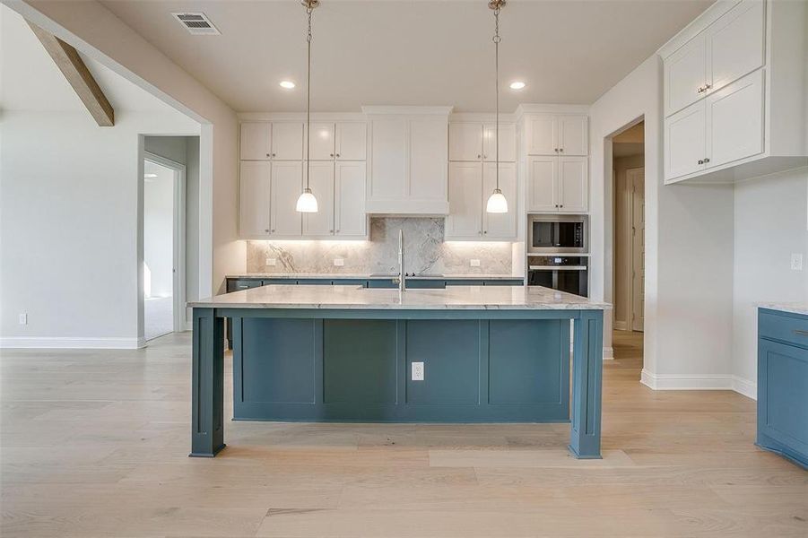 Kitchen with appliances with stainless steel finishes, hanging light fixtures, white cabinetry, and an island with sink