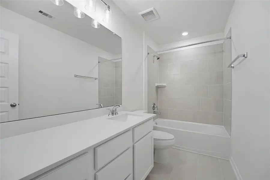 Secondary bath features tile flooring, bath/shower combo with tile surround, stained wood cabinets, beautiful light countertops, mirror, sleek fixtures and modern finishes.
