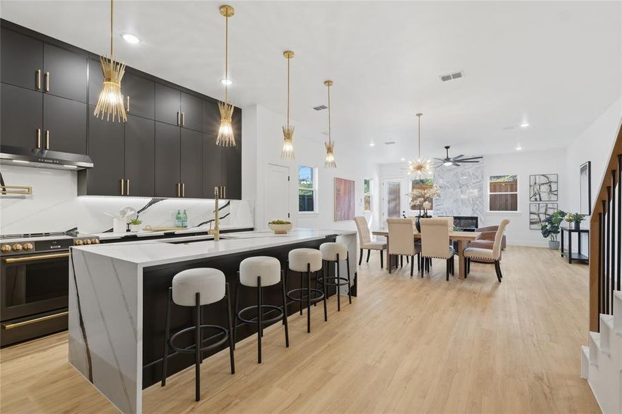 Kitchen featuring decorative light fixtures, dark cabinetry, gas stove, an island with sink, and a breakfast bar