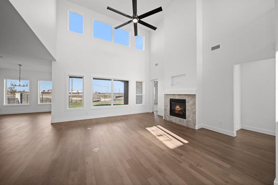 Unfurnished living room featuring a tiled fireplace, dark wood-style floors, a towering ceiling, ceiling fan, and a chandelier