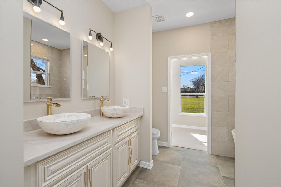 Luxurious master bathretreat with dual vesselsinks, elegant vanity, and aspa-like ambiance. Naturallight flows in, creating aserene start to your day."