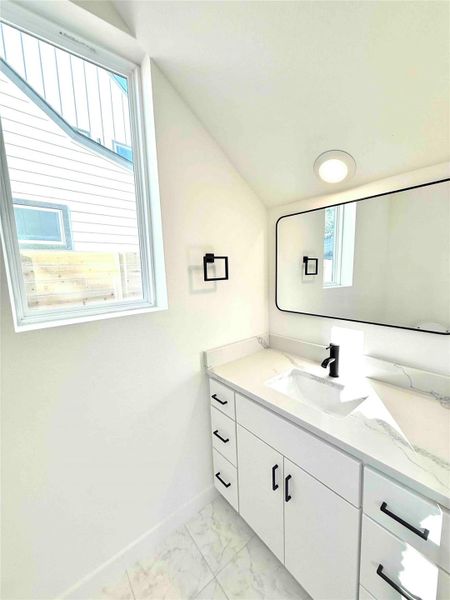 Bathroom with vanity, light marble finish floors, and vaulted ceiling