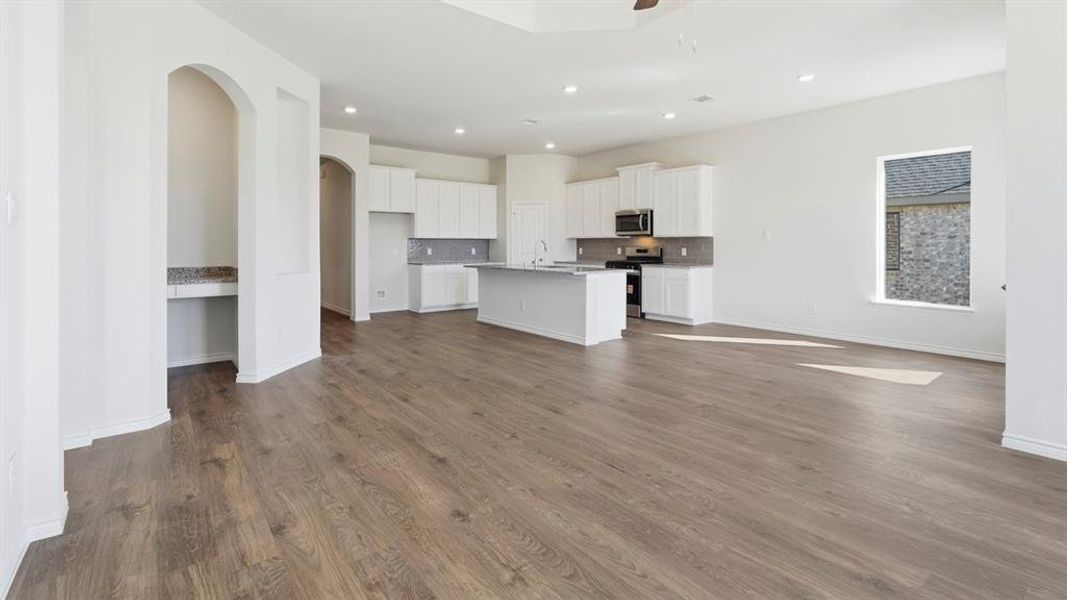 Open-concept living space featuring wood-look flooring, recessed lighting, and a kitchen with white cabinetry, a kitchen island, and stainless steel appliances Open-concept living space featuring wood-look flooring, recessed lighting, and a kitchen with white cabinetry, a kitchen island, and stainless steel appliances