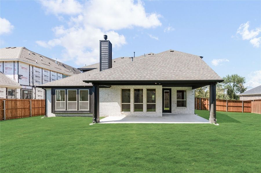 Rear exterior of single-story brick home with covered patio, chimney, and fenced backyard with green lawn Rear exterior of single-story brick home with covered patio, chimney, and fenced backyard with green lawn