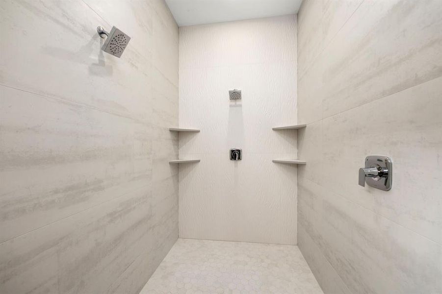 Luxurious primary bathroom shower featuring dual rainfall showerheads, sleek built-in shelving, and modern textured tile for a spa-inspired experience.