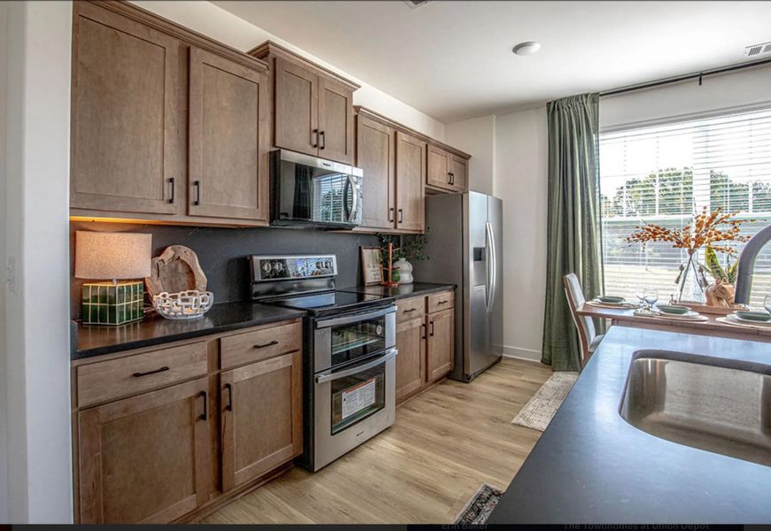 Kitchen with stainless steel appliances, light wood-style flooring, brown cabinets, and dark stone countertops
