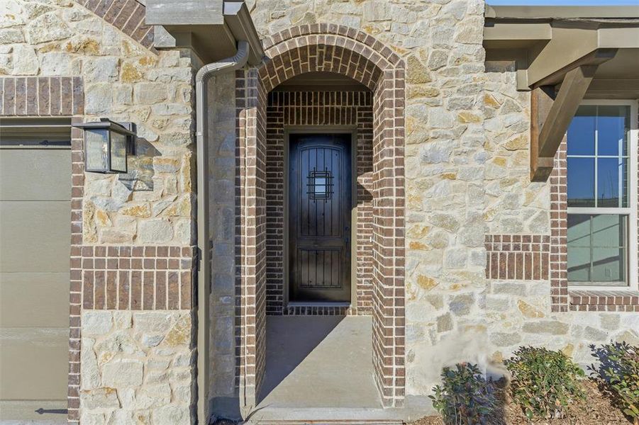 View of exterior entry with stone siding and brick siding