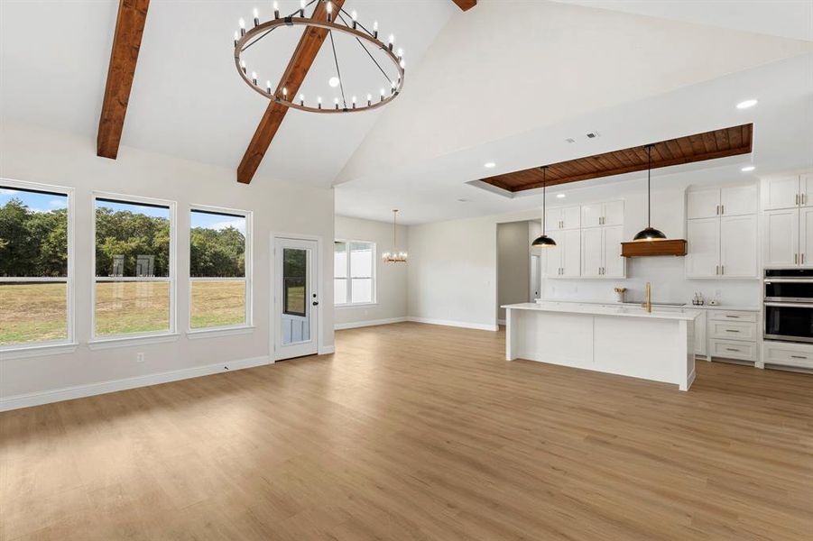 Unfurnished living room with a chandelier, light wood finished floors, high vaulted ceiling, recessed lighting, and beam ceiling